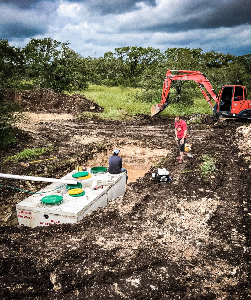 Crew setting a septic tank with an excavator nearby